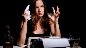 a woman holding a crumpled page in front of a type writer