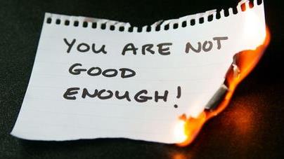 a paper inscribed with words 'you are not good enough' being burnt