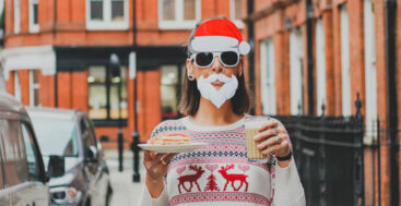 Woman in santa beard holding cookies and egg nog