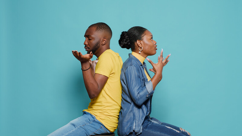 angry african american couple sitting back to back against a blue background