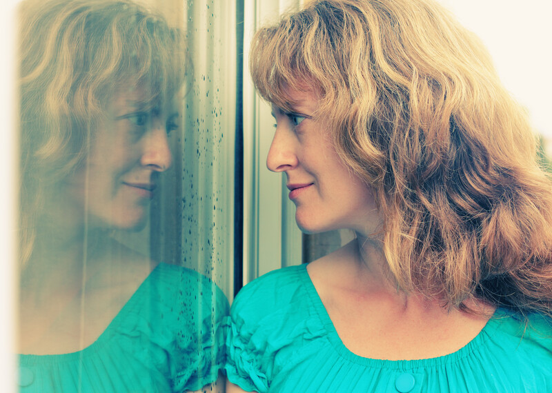 blonde woman with blue top looking at her refection in a window