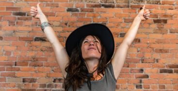 empowered woman with arms up standing in front of a brick wall