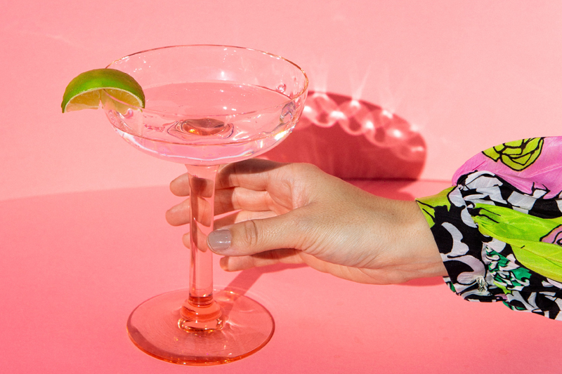 woman's hand holding a martini on a pink background