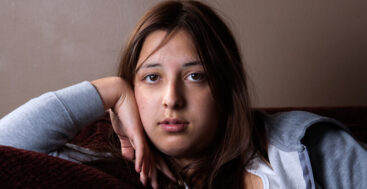 pensive teen sitting on couch resting head against arm