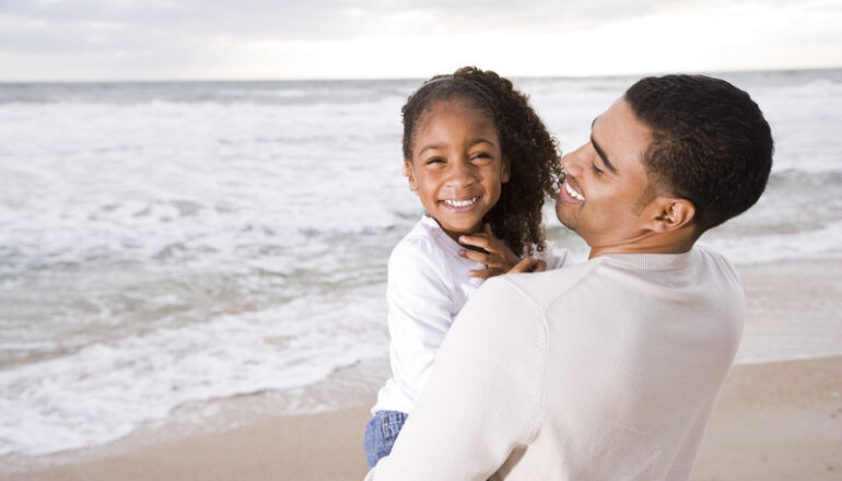 black father holiding child at the beach